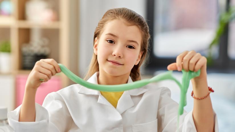 A young girl in a lab coat holding up green slime.