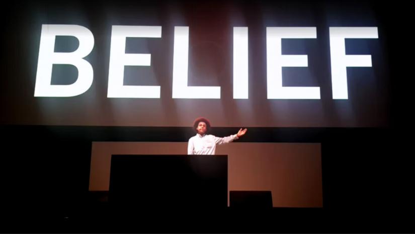 Solli Raphael speaking under a sign saying 'BELIEF'